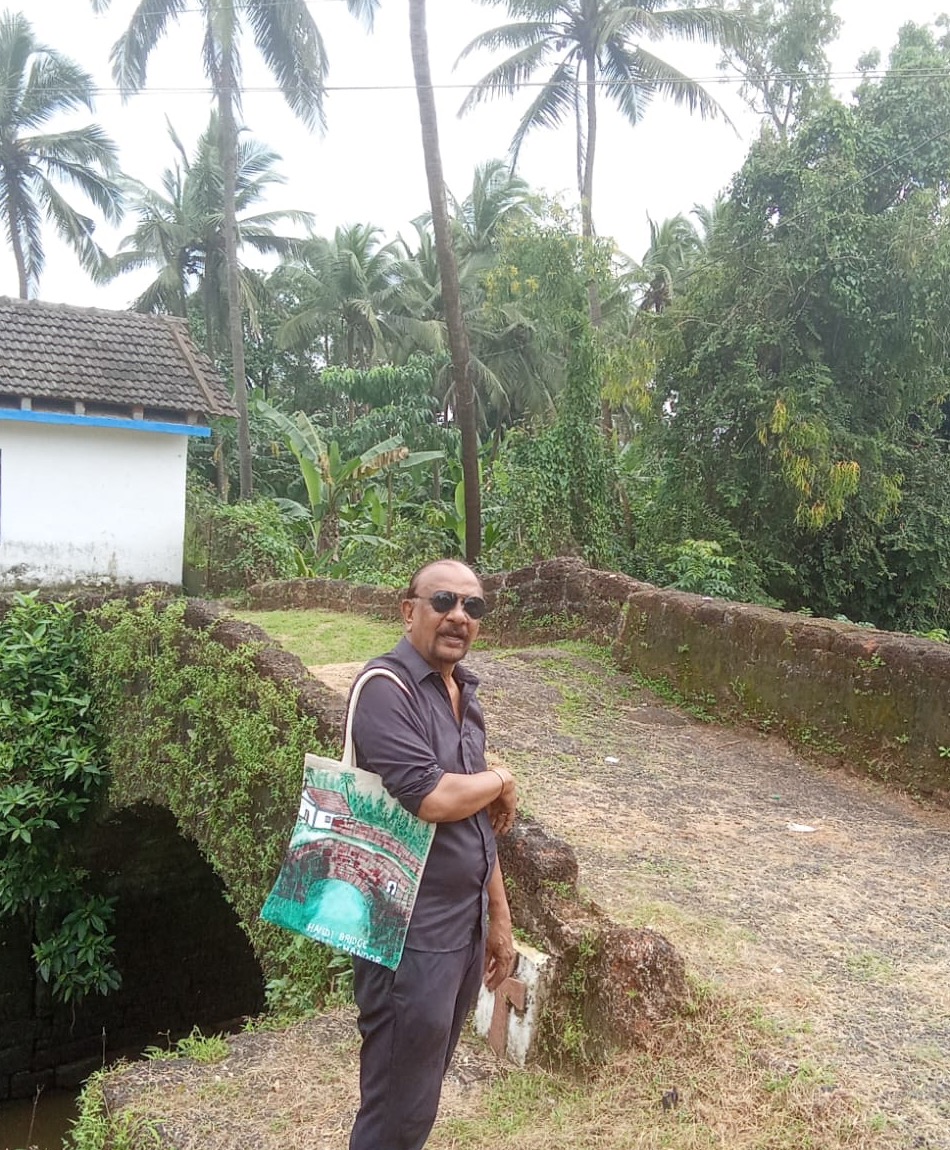 Irwin Antao standing on the Handi Bridge in Chandor, Goa, holding one of his hand-drawn tote bags